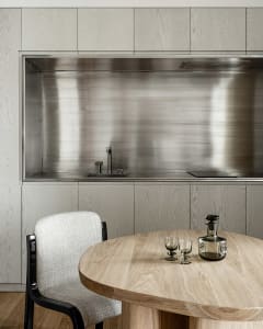 A minimalist modern kitchen with metallic finishes and a round wooden table.