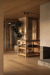 Modern minimalist kitchen with wooden flooring and furniture, featuring a wooden central island with a black countertop.