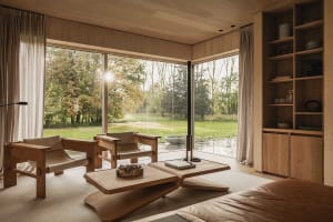 Modern minimalist living room with wooden furniture and large windows showing a scenic outdoor view.