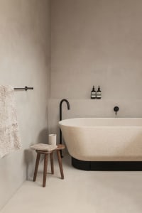A minimalist bathroom featuring a terrazzo bathtub and stool.