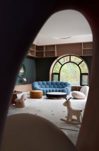 A modern playroom with a blue sofa, white rocking horse, and colorful floor