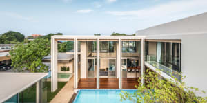 A modern residential house with glass walls and wooden flooring, featuring a swimming pool surrounded by greenery.