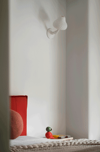 A minimalist bedroom featuring a red headboard, a white wall lamp, and a textured textile on the bed.