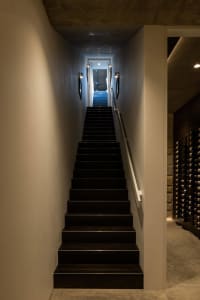 A modern staircase with black steps and a concrete wall, illuminated by wall-mounted sconces.