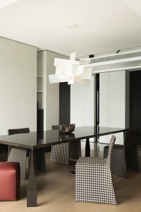 A modern dining room featuring patterned chairs and a sleek, black dining table, illuminated by a contemporary light fixture.