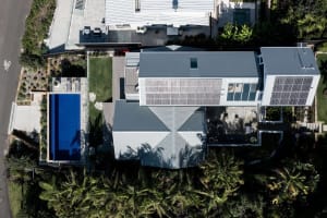 A modern residential exterior featuring metal, glass, and concrete materials with a landscaped garden.