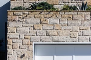 Modern stone exterior wall with greenery and a garage door.