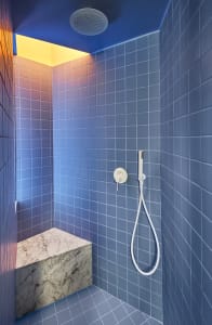 Minimalist bathroom shower area with blue tiles, marble bench, and modern fixtures.