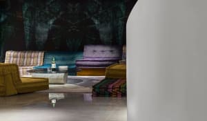 A modern lounge area with colorful upholstered furniture against a dark, abstract wall.