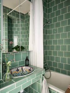 A modern bathroom with green ceramic tiles, a colorful sink, and a white bathtub.