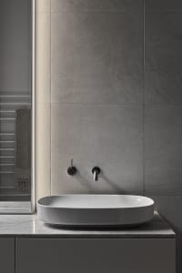 A modern bathroom with grey concrete walls, a minimalist white sink, and black fixtures.