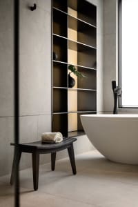 Modern bathroom interior with a concrete tile floor and wall, featuring a white freestanding bathtub and minimalist design el