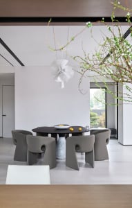 Modern dining room interior with minimalist black dining table, grey chairs, and a white flower arrangement.
