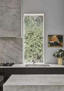 A modern kitchen with marble countertops and a large window overlooking greenery.