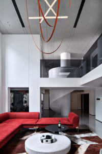Red sectional sofa, black coffee table, and circular concrete staircase in a modern lobby with large windows and concrete wal