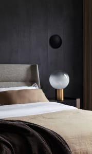 A modern minimalist bedroom with fabric bedding and a glass and metal lamp on a nightstand.