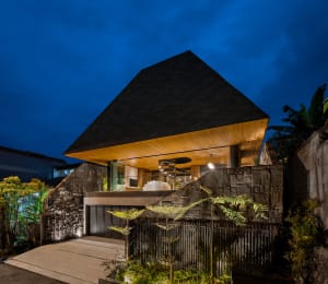 A modern house with a wooden facade and concrete foundation illuminated at night.