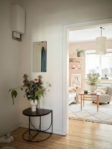A minimalist living room with wood flooring, a blush-colored accent wall, and a cozy seating arrangement.