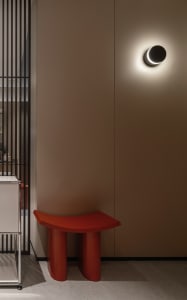 A minimalist modern interior with metal and wooden accents, featuring a red cylindrical bench and a contemporary wall lamp.