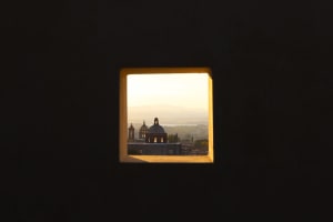 A square window frame reveals a view of a cityscape with domed structures and mountains in the distance, illuminated by a gol