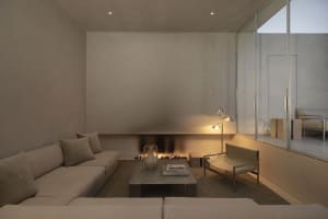 A minimalist living room featuring concrete walls and flooring with a cozy fireplace and comfortable seating.