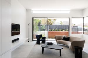 Minimalist living room with a neutral color palette, including a beige sofa, black armchair, and wooden coffee table.