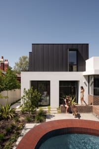 A modern residential house featuring a black concrete exterior with large windows and a swimming pool.