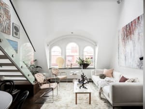 A modern minimalist living room with a white sofa and chairs, arched windows, and abstract paintings.