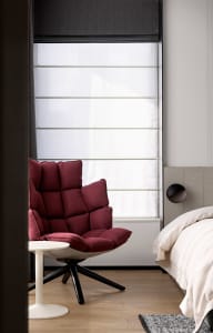A minimalist bedroom featuring a luxurious red upholstered chair, a comfortable bed with a neutral-toned quilt, and a modern,