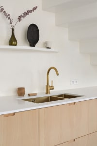 A minimalist residential kitchen with wooden cabinetry and a gold-finished sink.