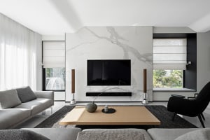 A modern living room featuring a marble accent wall with a flat-screen TV mounted on it, flanked by stereo speakers, and a wo