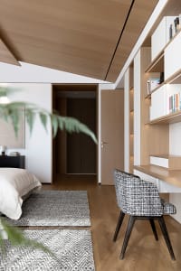 A modern minimalist bedroom with wooden walls, a black and white patterned chair, and a rug with geometric patterns.