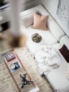 A modern white living room with a textured rug, white sofa with decorative pillows, and a coffee table with books and a candl