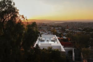 A rooftop with white furniture overlooking a city under a sunset sky.
