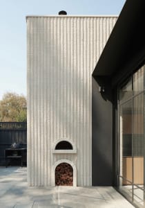 Modern, minimalist exterior of a building with a concrete finish, featuring a wood-fired oven and a firewood storage area.