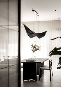 A modern dining room featuring a black metallic structure above a table with a vase of flowers.