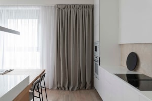 Modern minimalist kitchen featuring white cabinets, beige flooring, and a sleek, minimalist design with a single large window