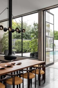 Modern industrial dining room with wood table, metal chairs, and large windows overlooking greenery.