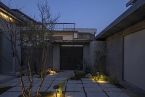 A modern residential entryway featuring a concrete pathway and walls, illuminated by outdoor lighting.