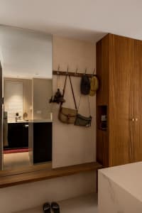 A minimalist entryway featuring a wall-mounted wooden coat rack with bags and hats, a marble bench, and a mirror reflecting a