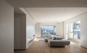 A minimalist living room with modern furniture and white walls, featuring a large window with a view of the city.