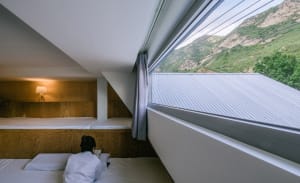 Minimalist bedroom with wooden walls and a view of the mountains outside a large window.