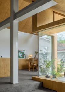 A modern home office with wooden walls, concrete floor, and a desk with a lamp and a chair.