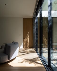 A modern living room featuring a window with a shadow cast on the plank flooring, creating a minimalist and serene atmosphere