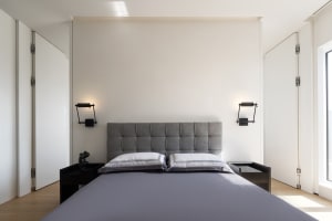 Modern minimalist bedroom with a grey upholstered headboard, white bedding, and black sconces on either side of the bed.