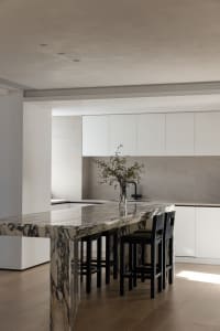 Modern minimalist kitchen with marble countertops and black stools.
