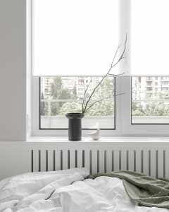 A minimalist bedroom with a white blanket and gray blanket on a bed, featuring a vase with a branch and a bird figurine on a 