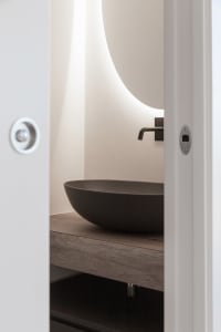 Modern bathroom featuring a sleek, dark-colored concrete sink and illuminated oval-shaped mirror above a floating wooden coun