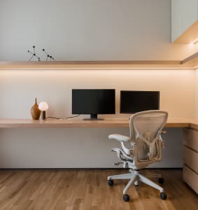 Modern minimalist home office featuring a wooden desk and chair, two monitors, and a sleek design.