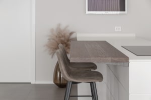 Modern minimalist kitchen featuring a wooden table with two stools and a vase of dried flowers.